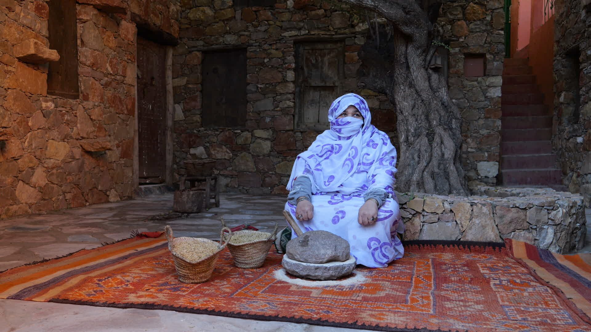 Amazigh woman grinding grain on a stone quern, Morocco — El Guayota